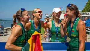 Keturios besijuokiančios Lietuvos irklavimo rinktinės sportininkės su medaliais ir vėliava po varžybų.
