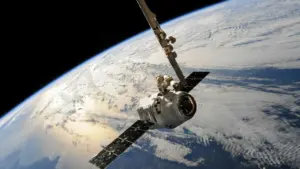 Baltas SpaceX erdvėlaivis skrieja orbitoje virš Žemės planetos su matomais debesimis ir horizontu.