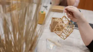 Moteris rankose laiko rankų darbo šiaudinį geometrinį žaislą, sukurtą tradicinių amatų dirbtuvių metu.