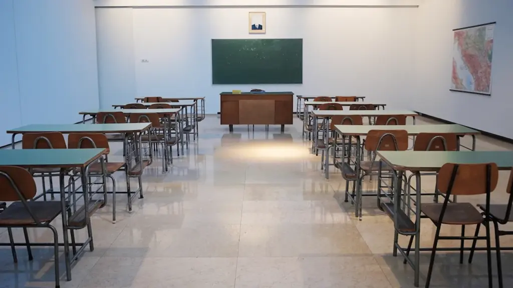 Tuščia klasė su mediniais suolais ir žalia lenta švietimo įstaigoje.