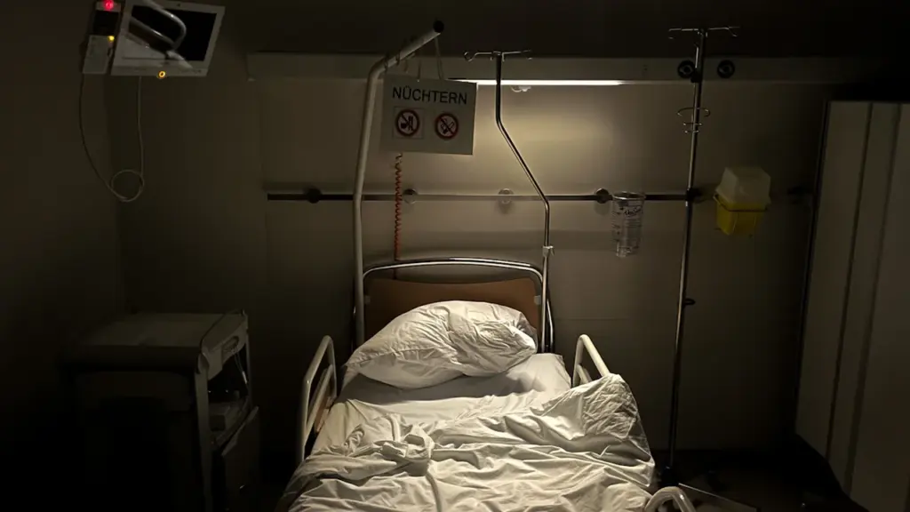 Tuščia ligoninės lova su prijungta medicinine įranga pritemdytame kambaryje