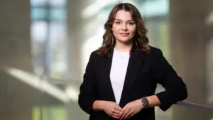 Profesionaliai atrodanti jauna moteris šviesiais plaukais, vilkinti juodą švarką bei baltus marškinėlius.