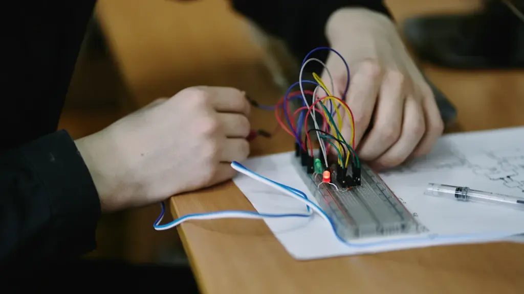 Studentas atlieka laboratorinius elektros inžinerijos darbus su laidų schema ir plokšte
