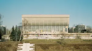 Modernus stiklinis pastatas prie upės Vilniuje, atspindintis šiuolaikinę miesto aplinką rudenį.